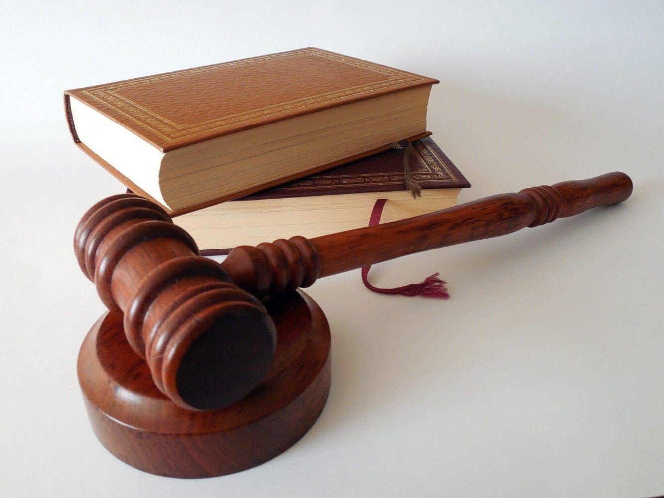 A dark brown wooden gavel on its sound block, with two stacked, gold-embossed hardcover books behind it, all on a white surface.