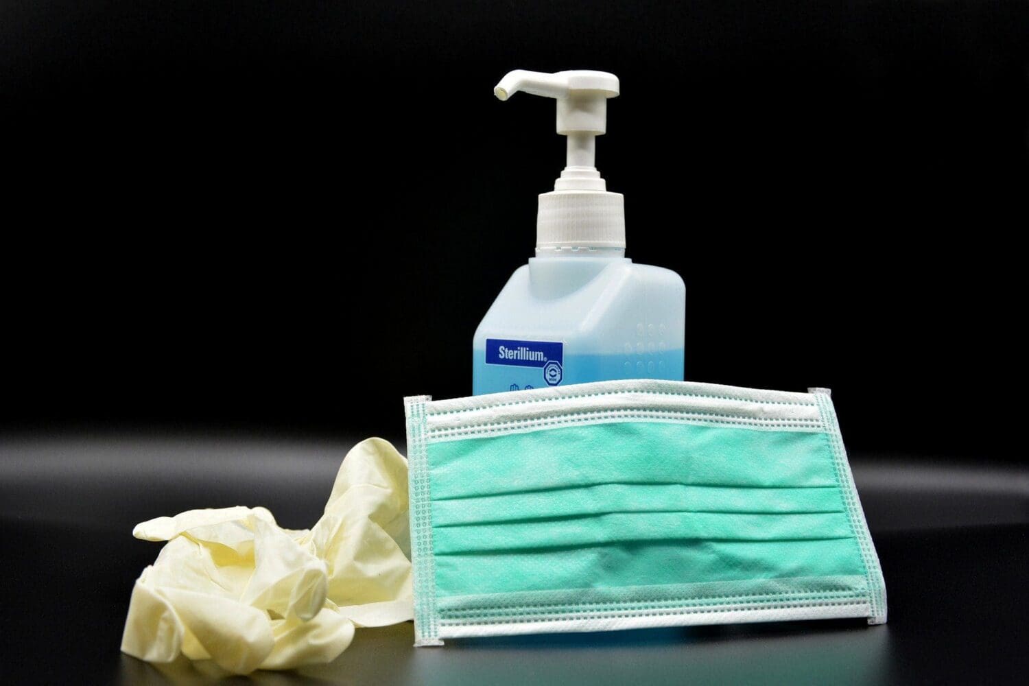 Hand sanitizer, a green surgical mask, and yellow gloves on a black background.