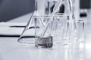 Clear glass laboratory beakers and flasks on a light surface. One beaker contains two liquid layers and a glass dropper.
