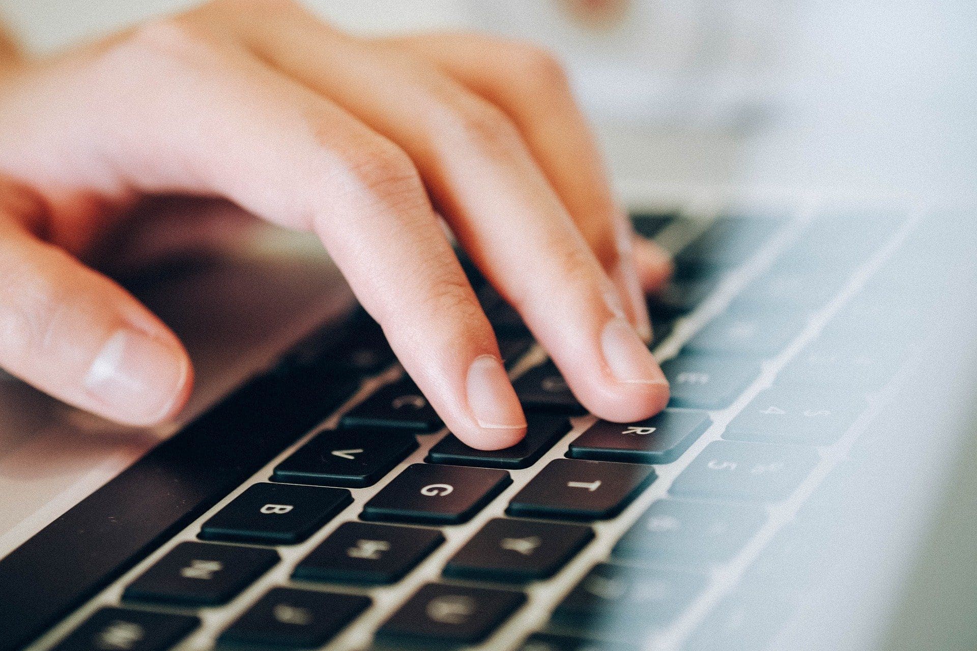 Adherent (formerly Compliance & Risks). Close-up of a hand with light skin tone typing on a black laptop keyboard, with fingers resting on the G, H, and J keys.