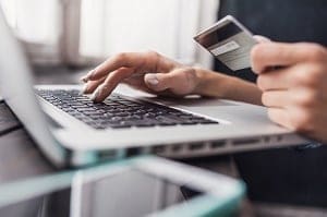 Close-up of hands typing on a laptop keyboard while holding a credit card.