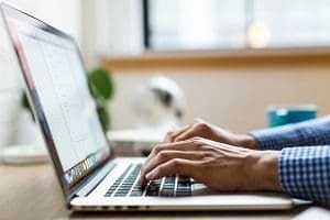 Close-up of hands typing on a silver laptop keyboard.
