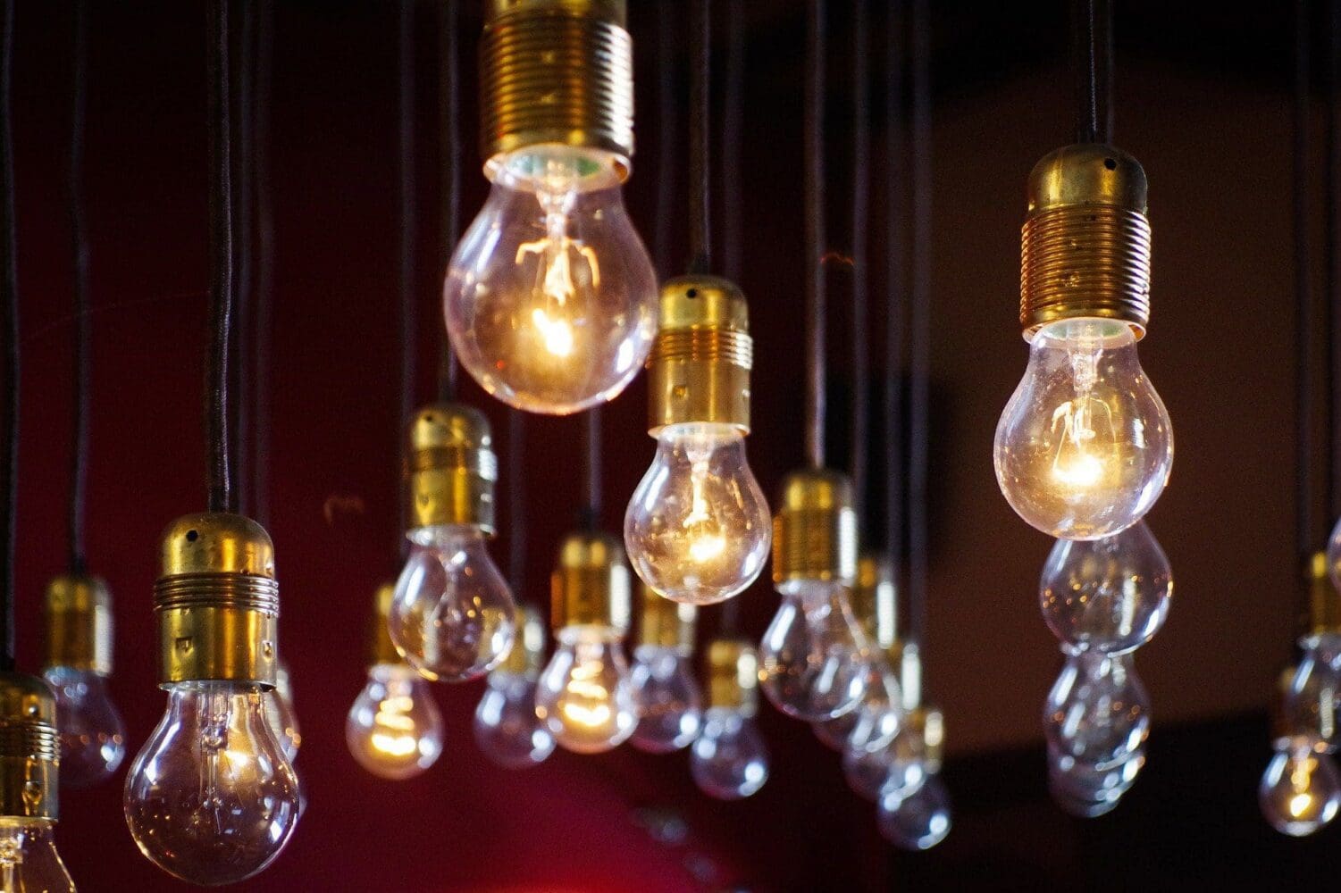 A cluster of glowing vintage-style light bulbs with brass bases hanging from dark cords against a dark background.