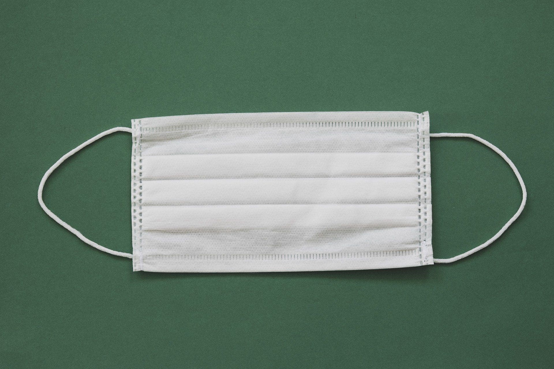 A white disposable face mask with ear loops on a dark green background.