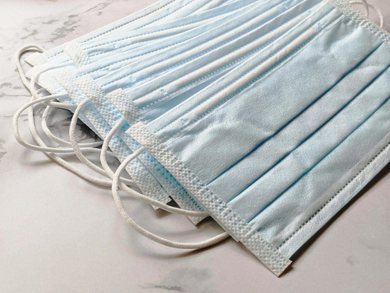 Several light blue disposable surgical masks stacked on a light-colored surface.