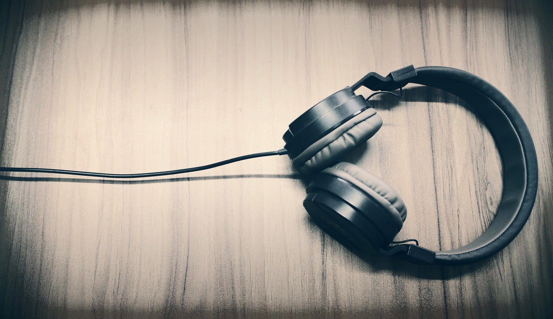 Adherent (formerly Compliance & Risks). Dark over-ear headphones with a cable on a light wooden surface.