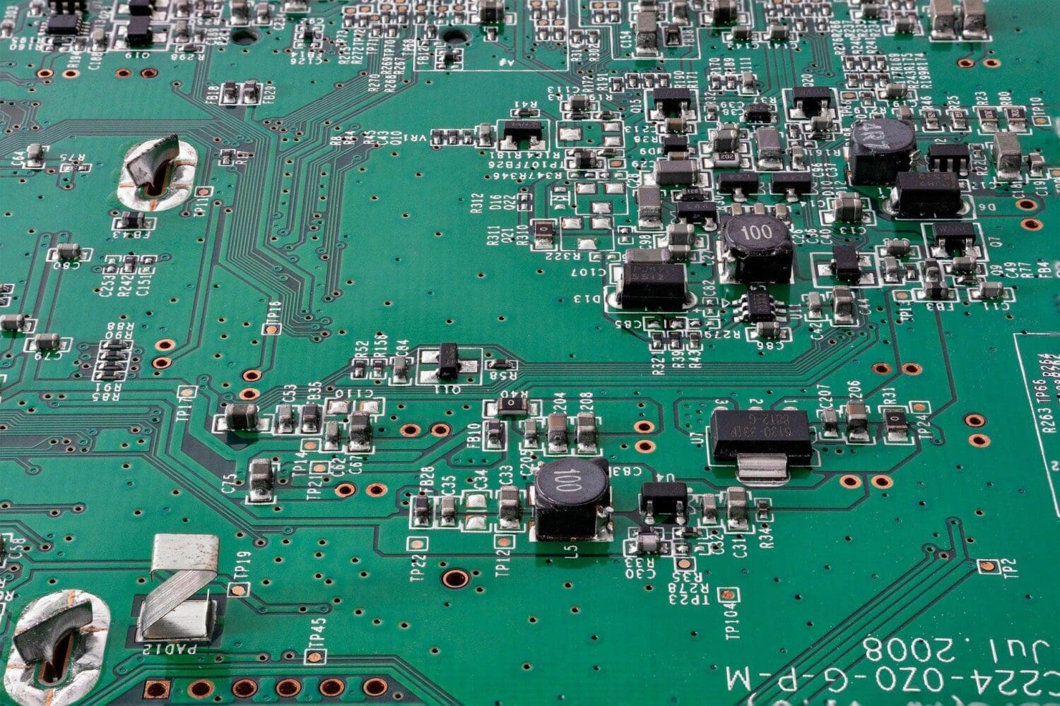Close-up of a green printed circuit board (PCB) covered with various electronic components like resistors, capacitors, inductors, and integrated circuits. Traces and silkscreen markings are visible, along with text 'JUL.2008'.