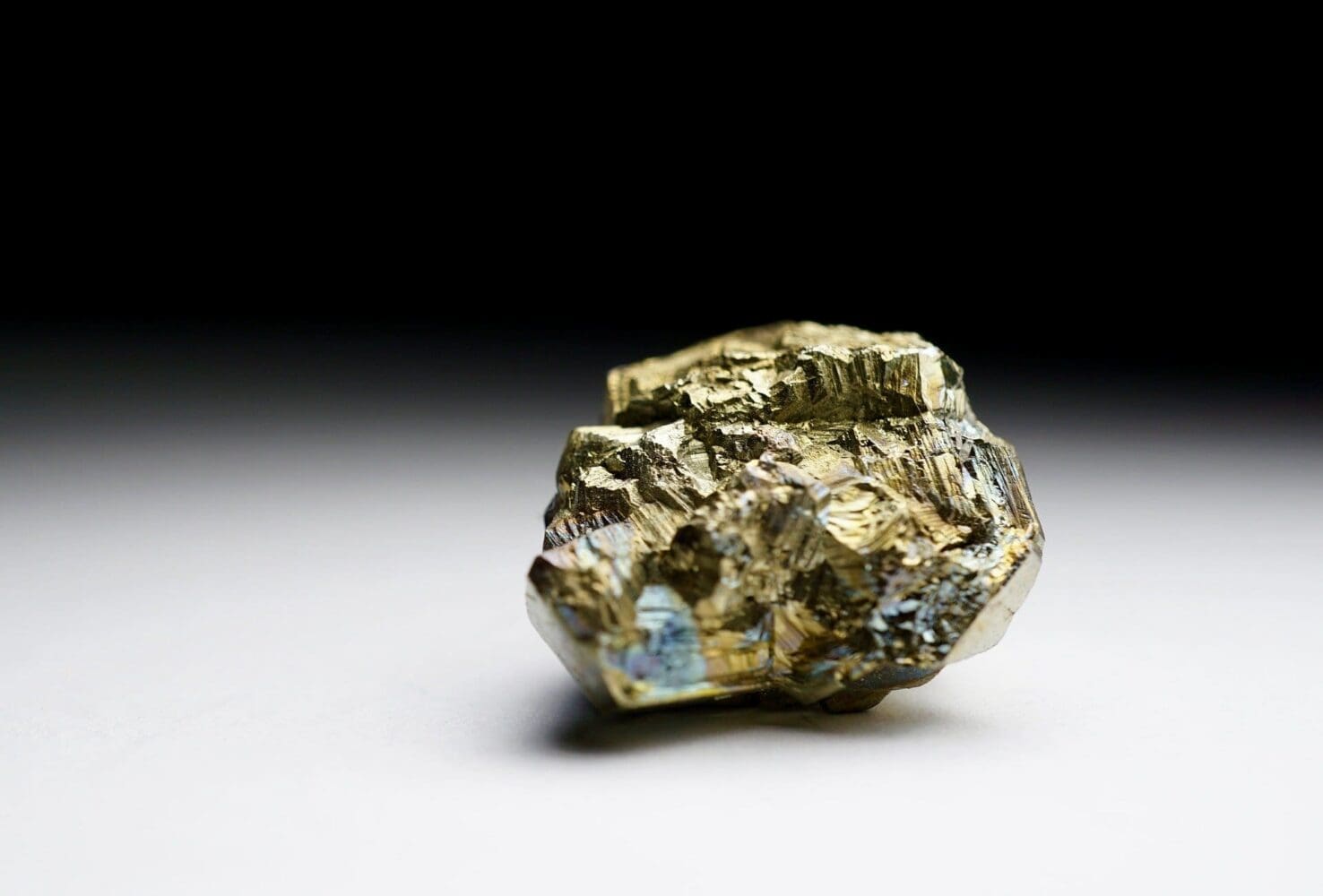 A metallic, brassy yellow pyrite mineral specimen with iridescent blue and purple reflections, on a white and black gradient background.