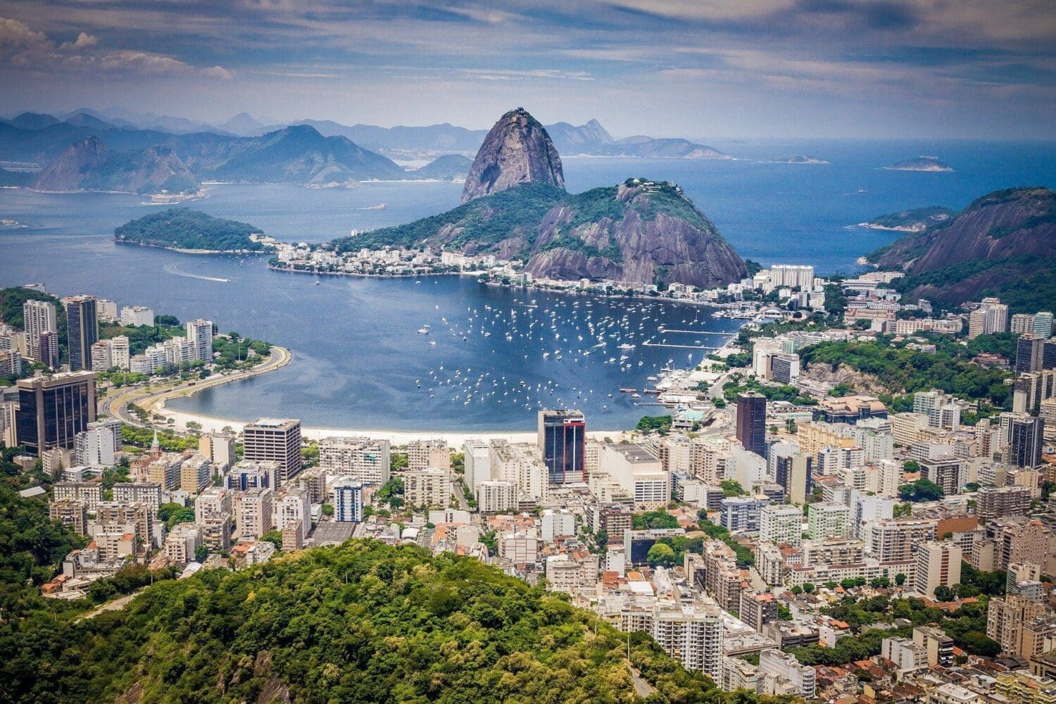 Aerial view of Rio de Janeiro with Sugarloaf Mountain, a bay with boats, and city buildings.
