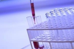 A pipette dispenses red liquid into a test tube held in a lab rack.