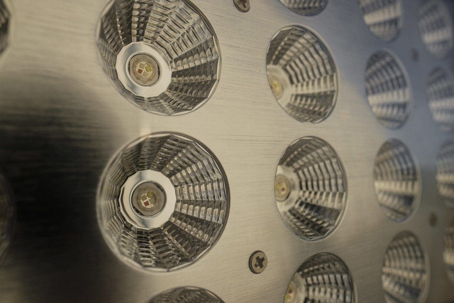 Close-up of a brushed metal panel featuring multiple circular LED lights, each with a central multi-color chip and a clear, faceted lens.
