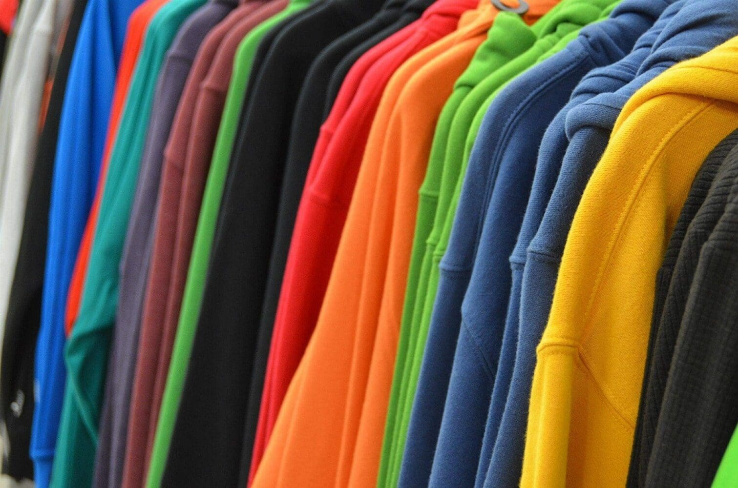A close-up of many colorful hoodies hanging on a rack, including blue, red, orange, green, yellow, and black.