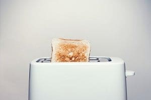 A slice of golden-brown toast pops out of a white toaster.
