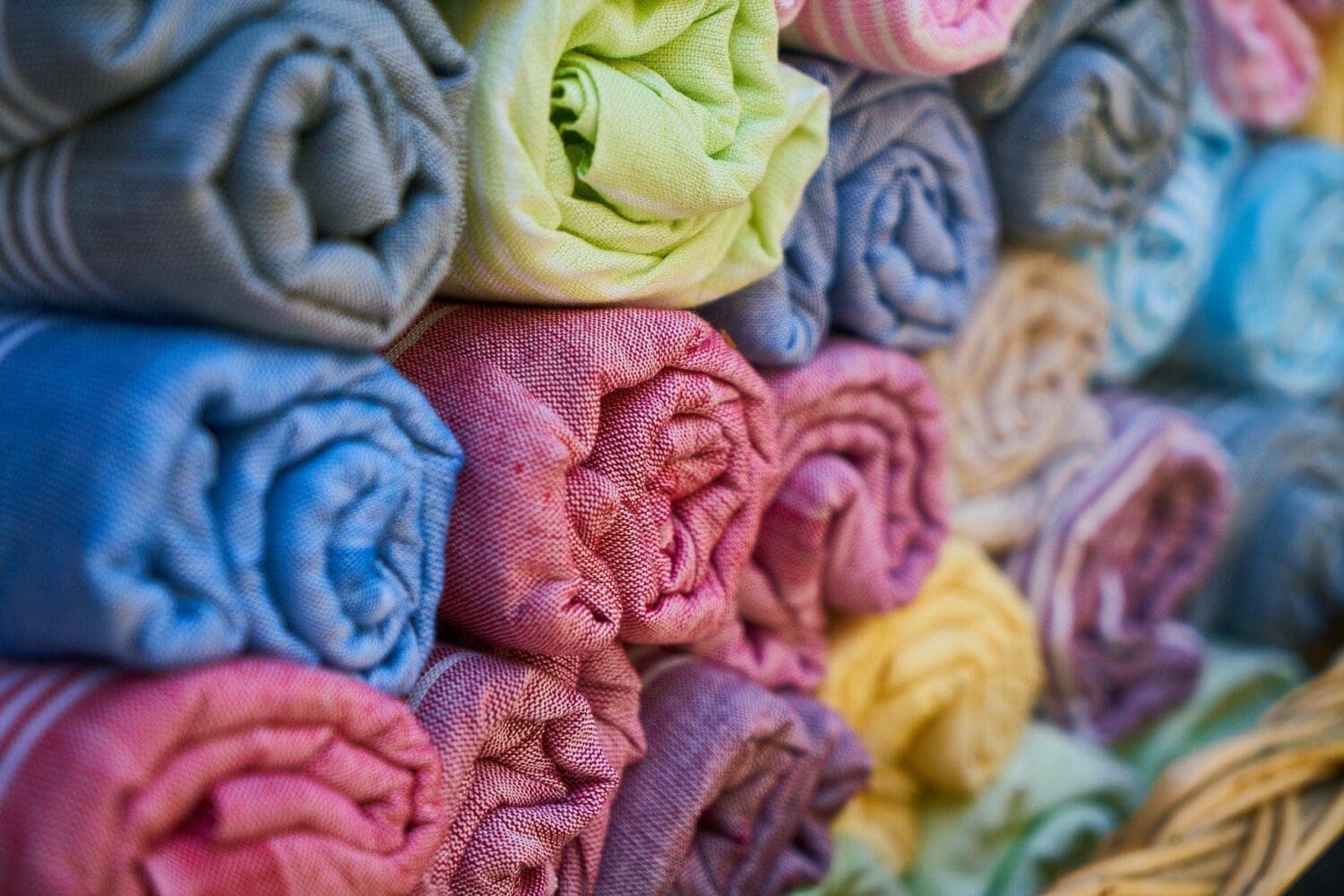 Close-up of many rolled-up textiles in a variety of colors, including blue, green, pink, red, purple, and yellow, stacked neatly.