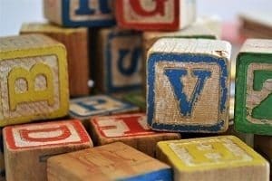Close-up of a pile of worn wooden alphabet blocks with various colored letters like V, B, and D.