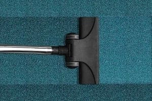 A black vacuum cleaner head on a teal carpet, showing distinct vacuum lines on the left side.