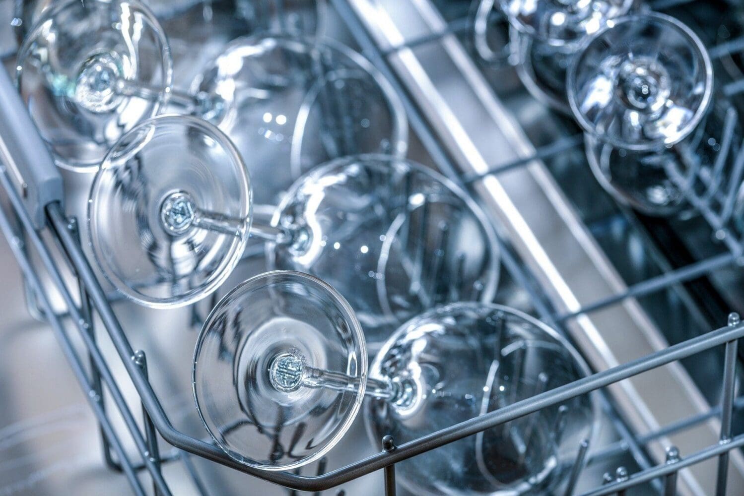 Close-up of clean, clear wine glasses upside down in a dishwasher rack.