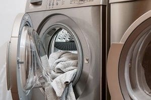 A silver front-loading washing machine with its door open, showing light-colored towels inside.
