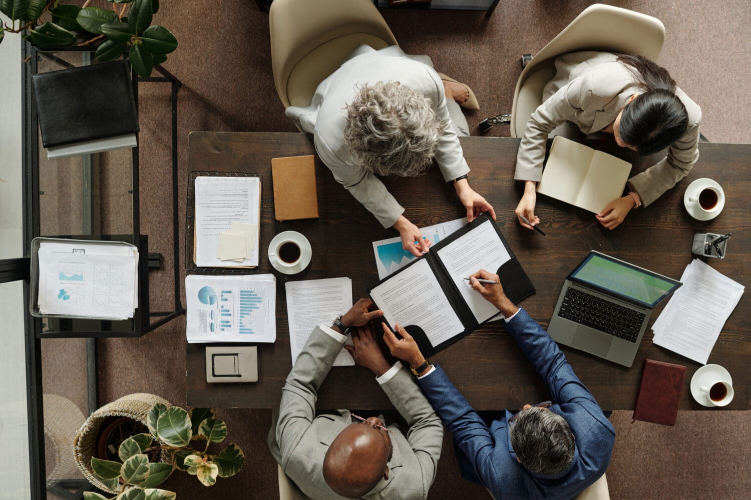 Overhead view of four business professionals at a wooden table, reviewing and signing documents.