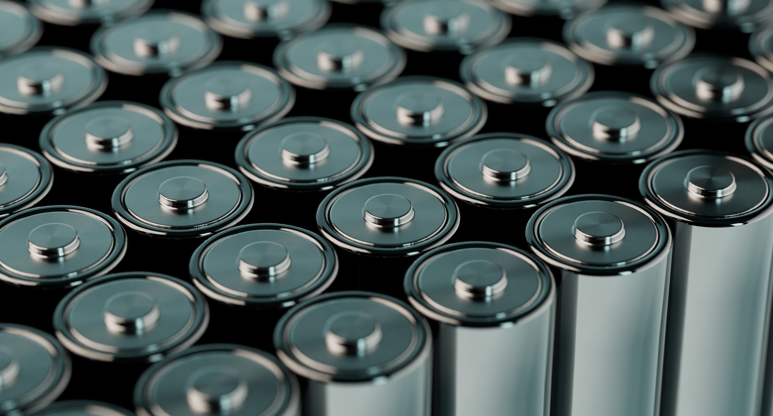 A close-up view of many silver cylindrical batteries with metallic tops arranged in rows on a dark background.