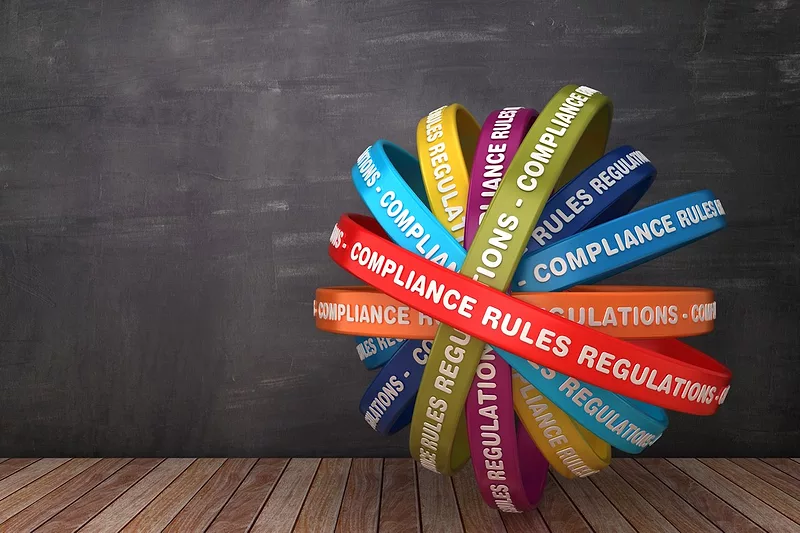 Colorful, intertwined bands with text like 'COMPLIANCE', 'RULES', and 'REGULATIONS' against a dark background and wooden floor.
