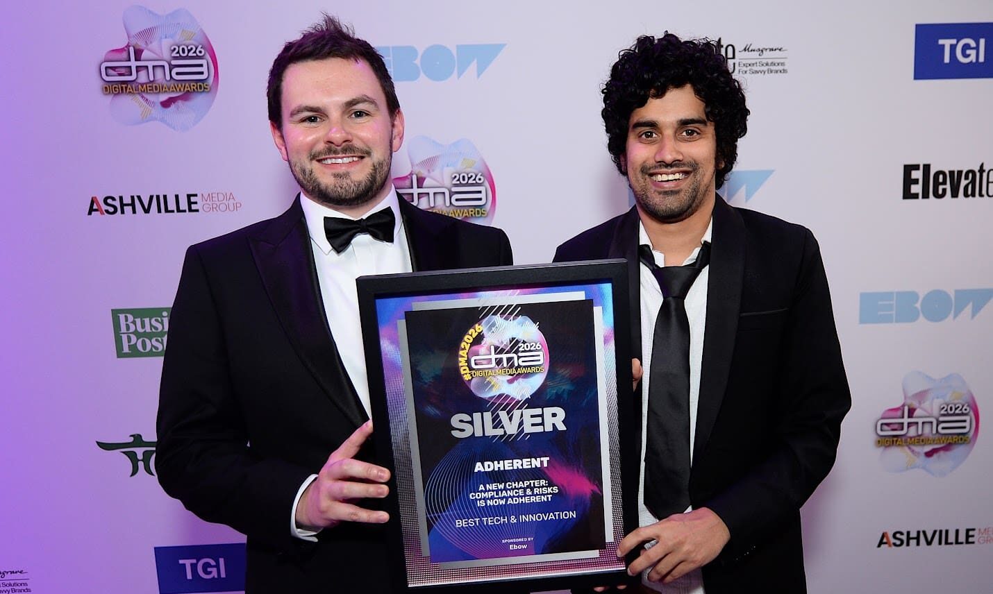 Two smiling men in tuxedos hold a silver award from the 2026 Digital Media Awards for 'Best Tech & Innovation' by Adherent.
